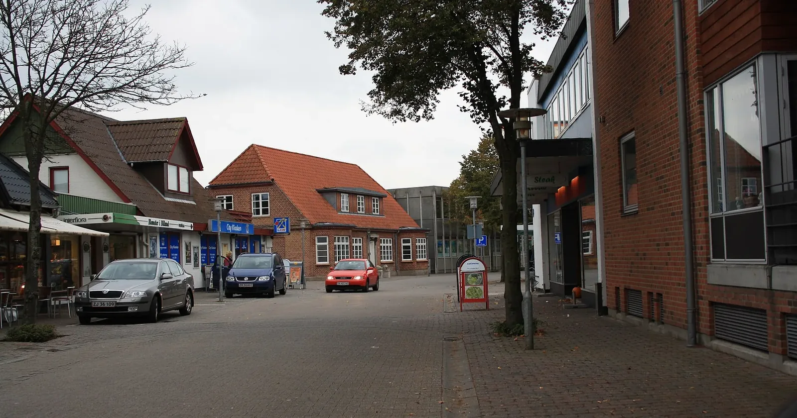 Hovedgaden i Billund med butikker, trær og biler