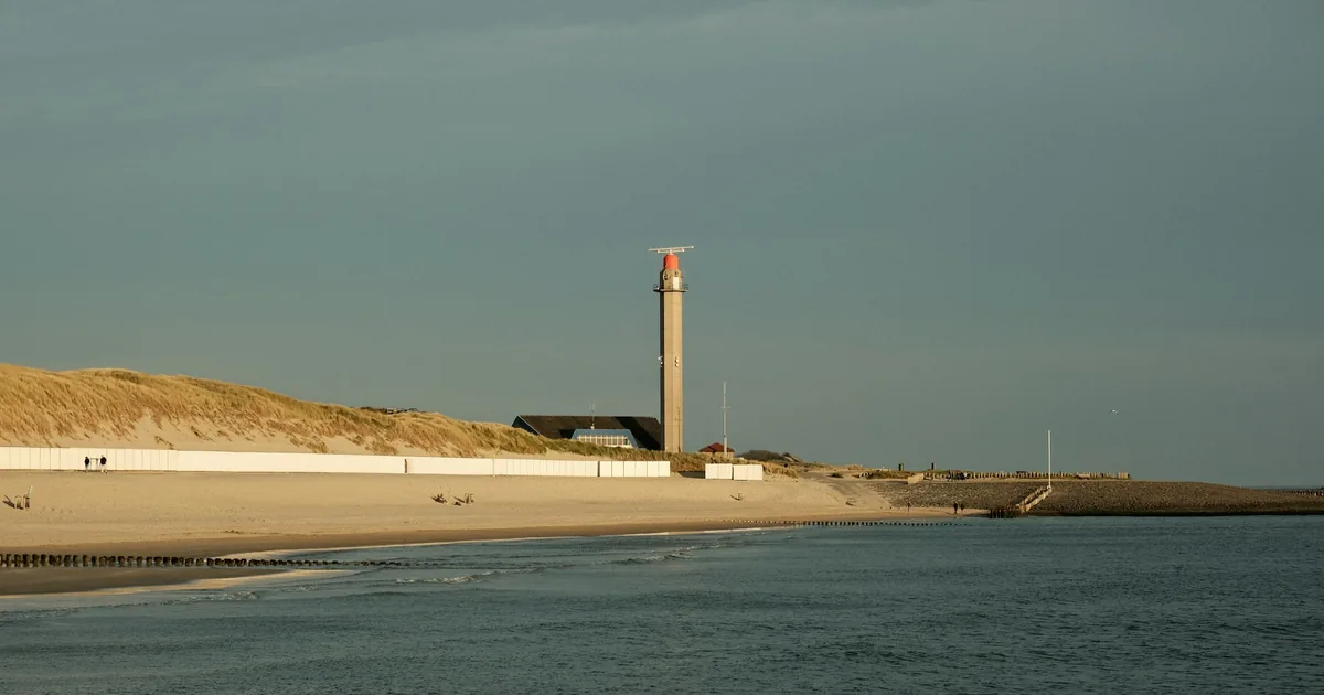 Fyrtårn på en sandodde ved havet under en lys himmel