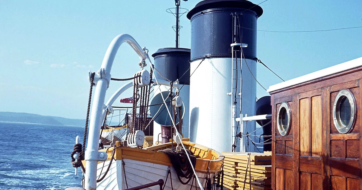 Dekket på et skip med skorsteiner og rekkverk, med havet bak
