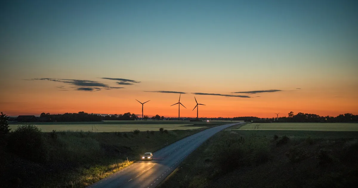 Vei gjennom flatt landskap i solnedgang, med vindmøller i horisonten
