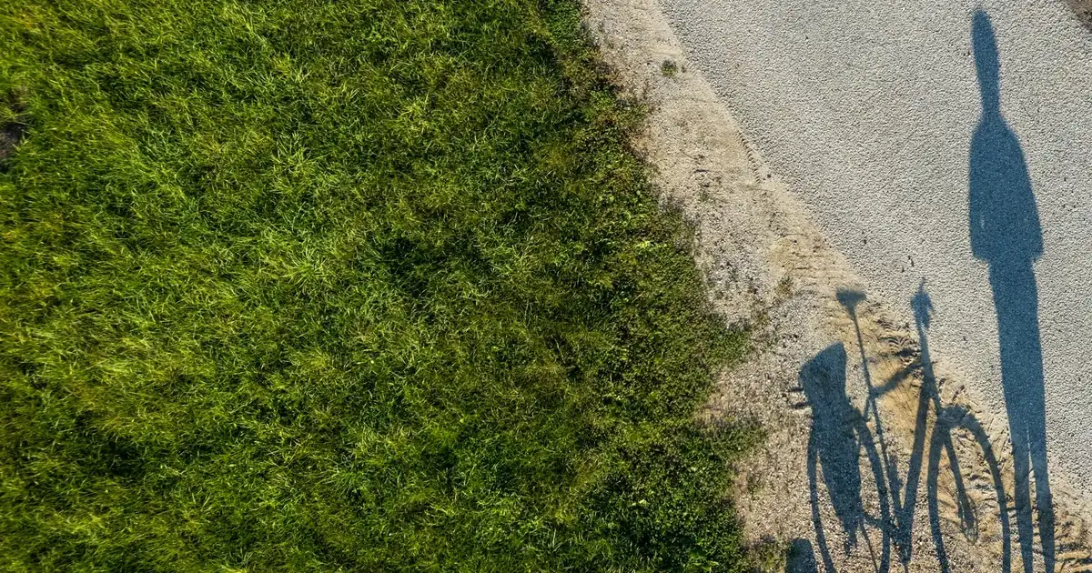 Skyggene av to syklister på en sykkelsti langs en gressplen