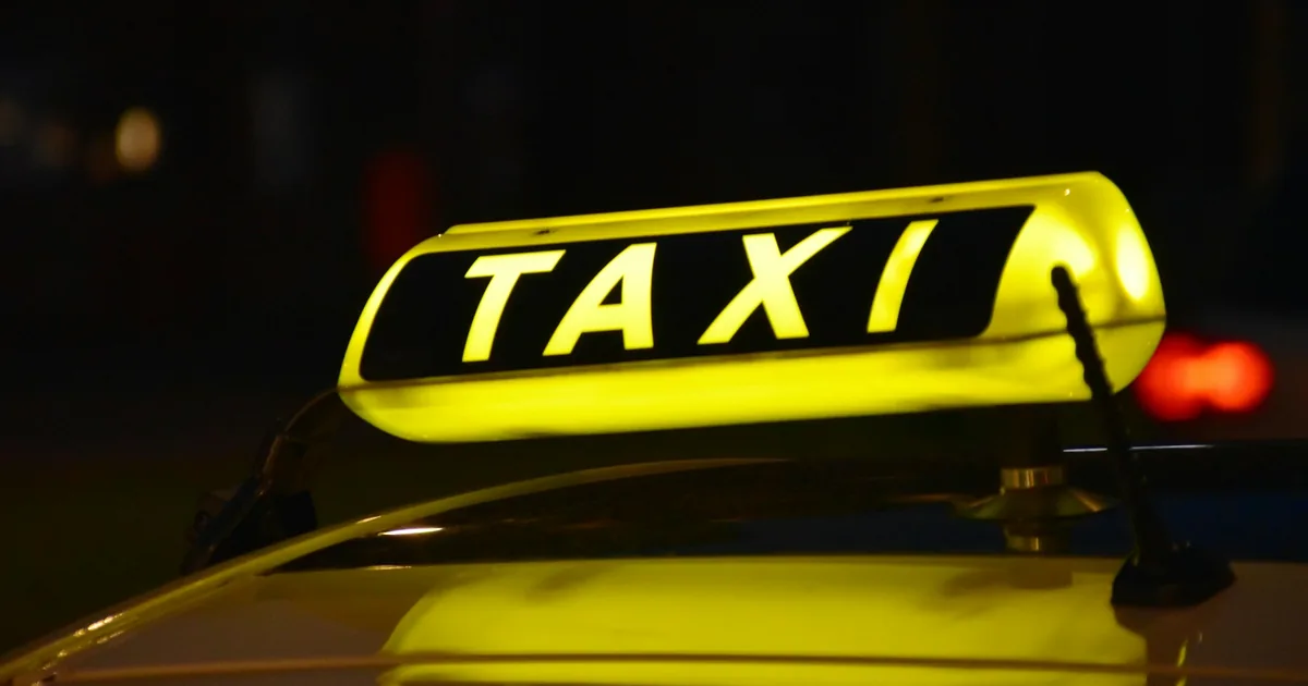 Opplyst taxiskilt på taket av en drosje om kvelden