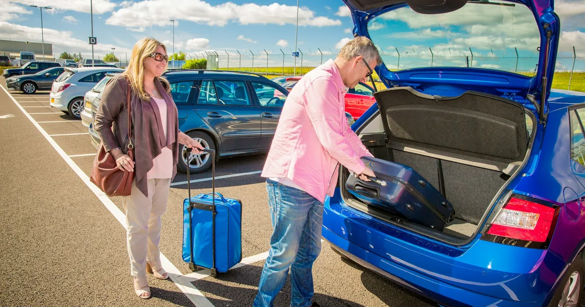 To voksne som pakker kofferter i bagasjerommet på en blå bil på en parkeringsplass